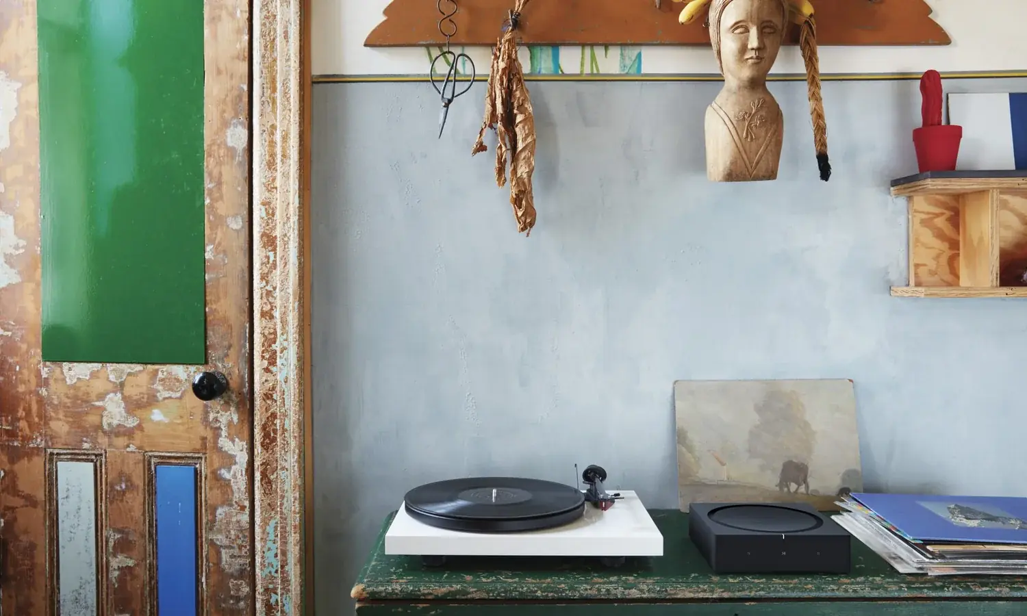 A turntable and a Sonos Amp on a weathered green cabinet against a blue plaster wall