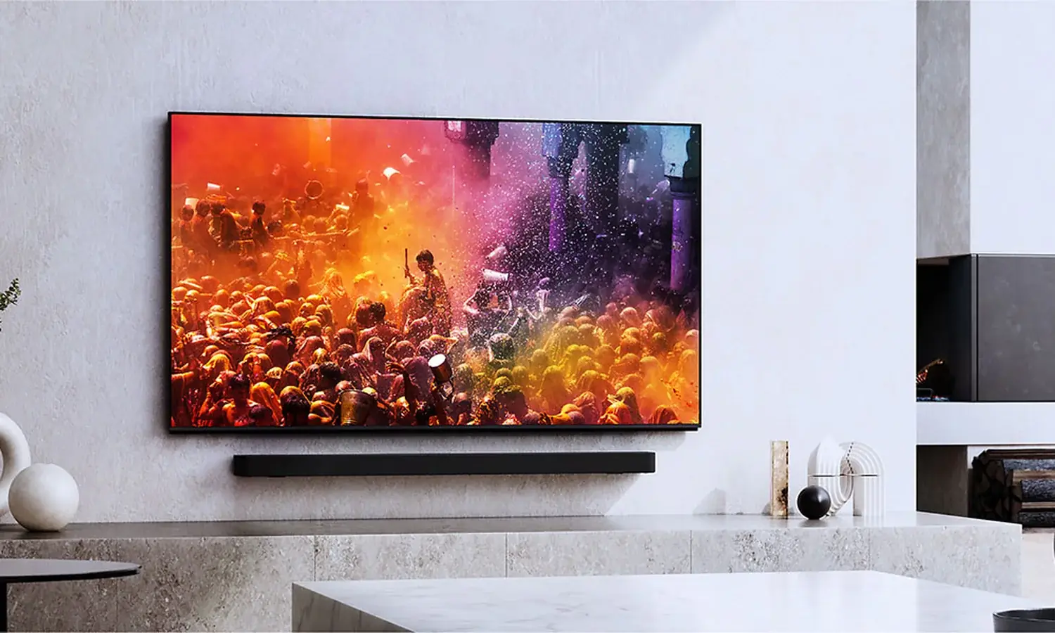 A Sony Bravia television on a pale stone wall above a soundbar, showing a crowd in clouds of colored powder