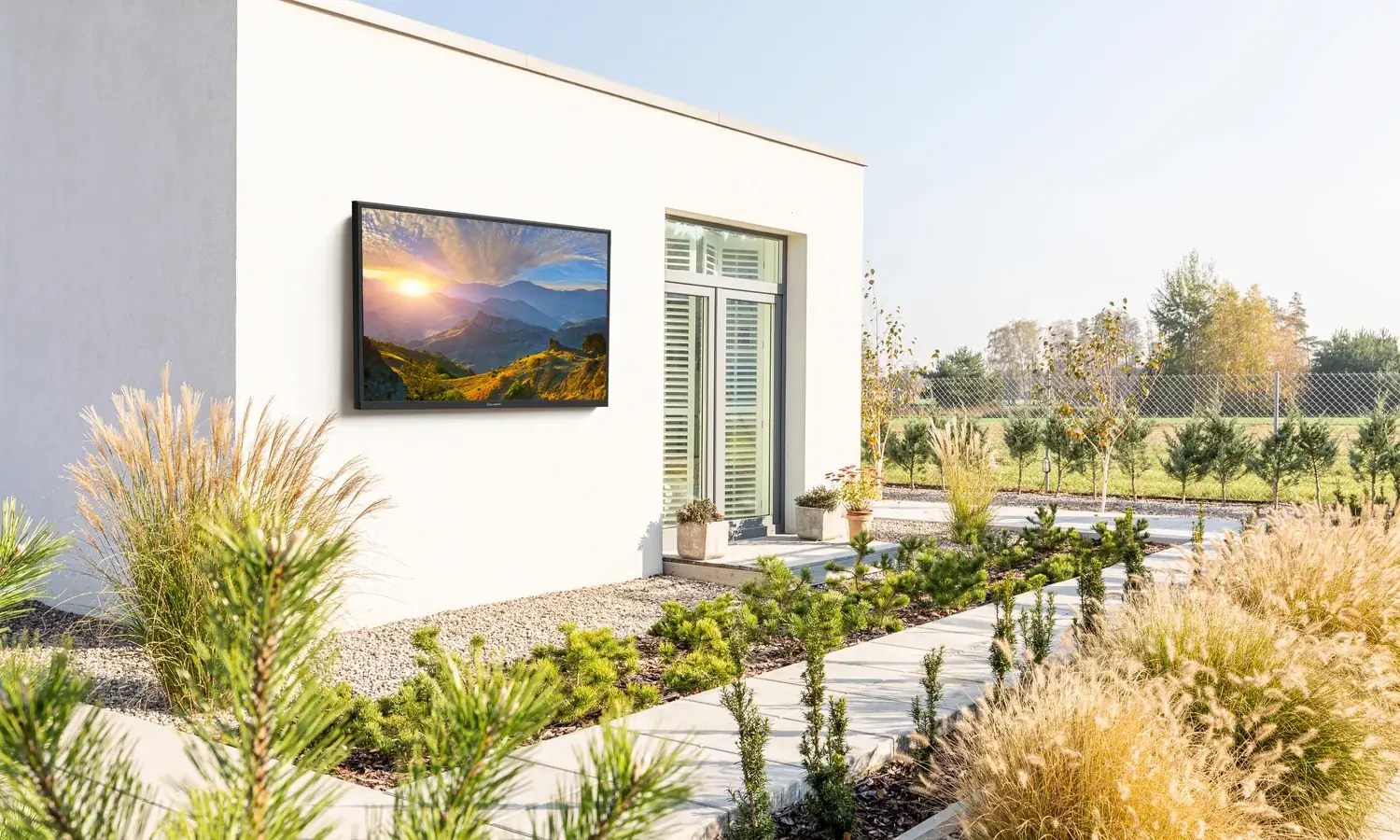 A television on the white wall of a house above a garden bed