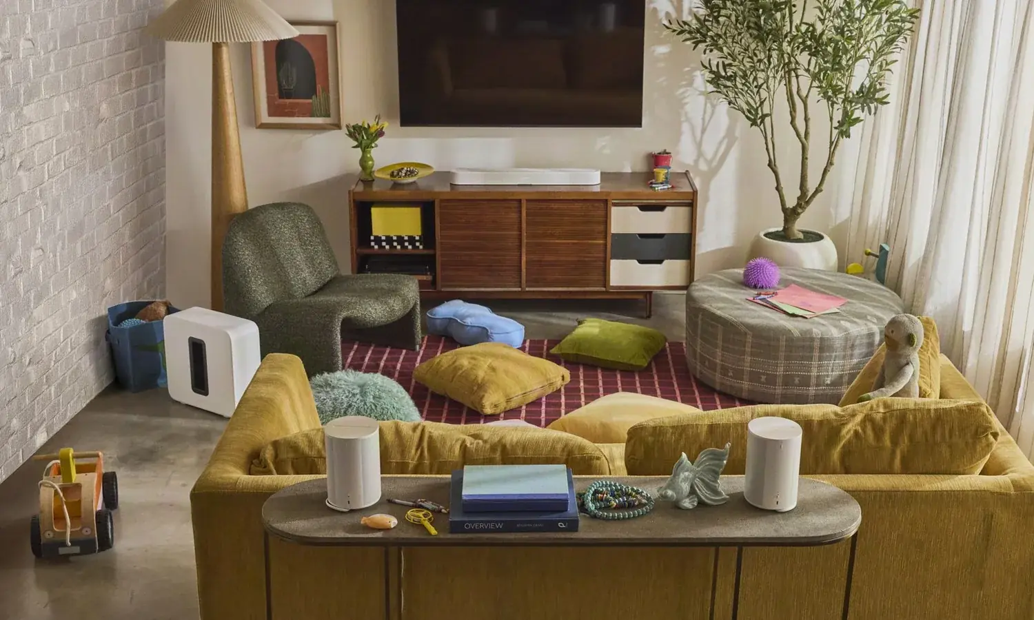 A living room with a wall-mounted television above a walnut credenza, a Sonos Sub and two Era speakers on the sofa table