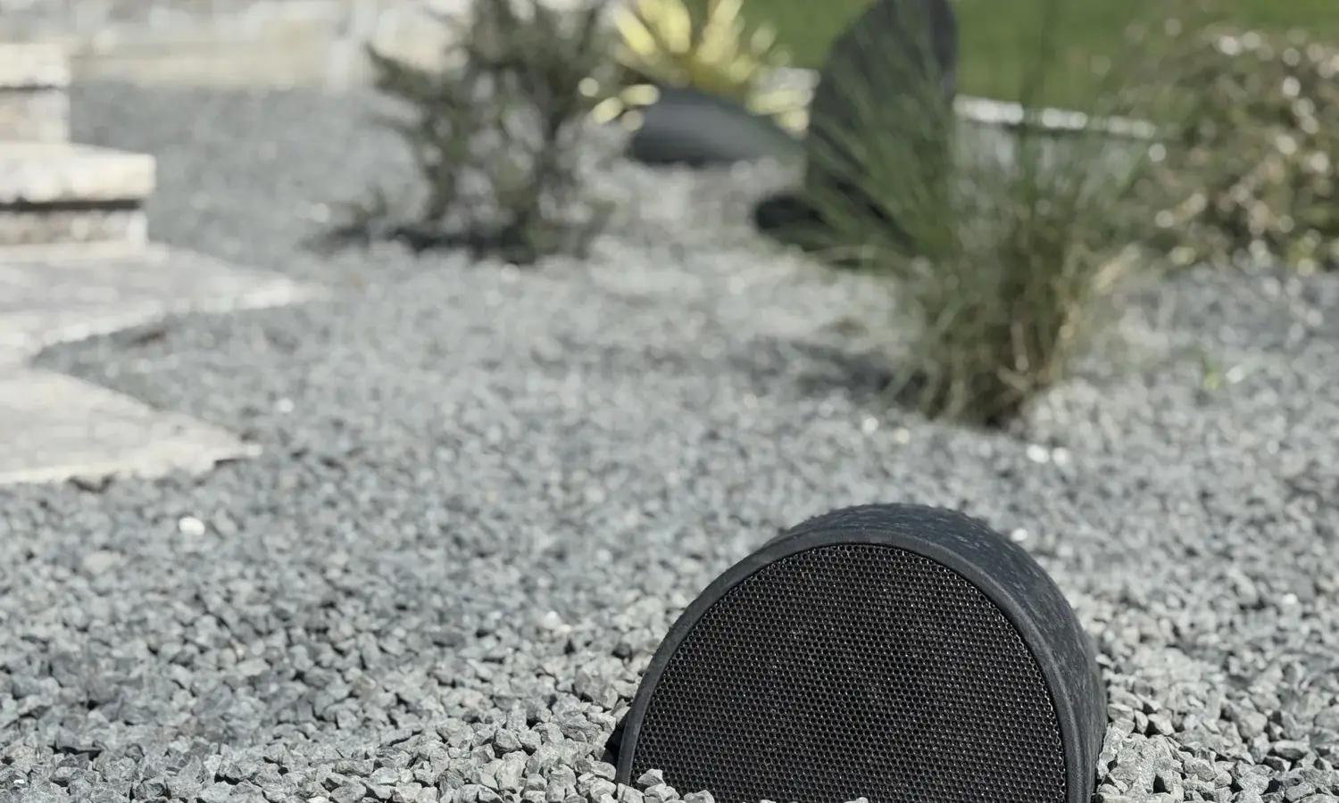 A low landscape speaker set into gravel at grade