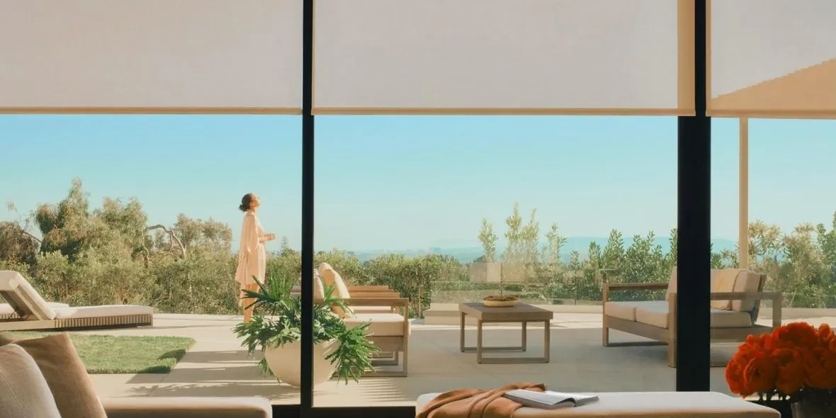 A terrace behind a wall of glass with roller shades lowered to the head of the opening, the view held and the glare cut