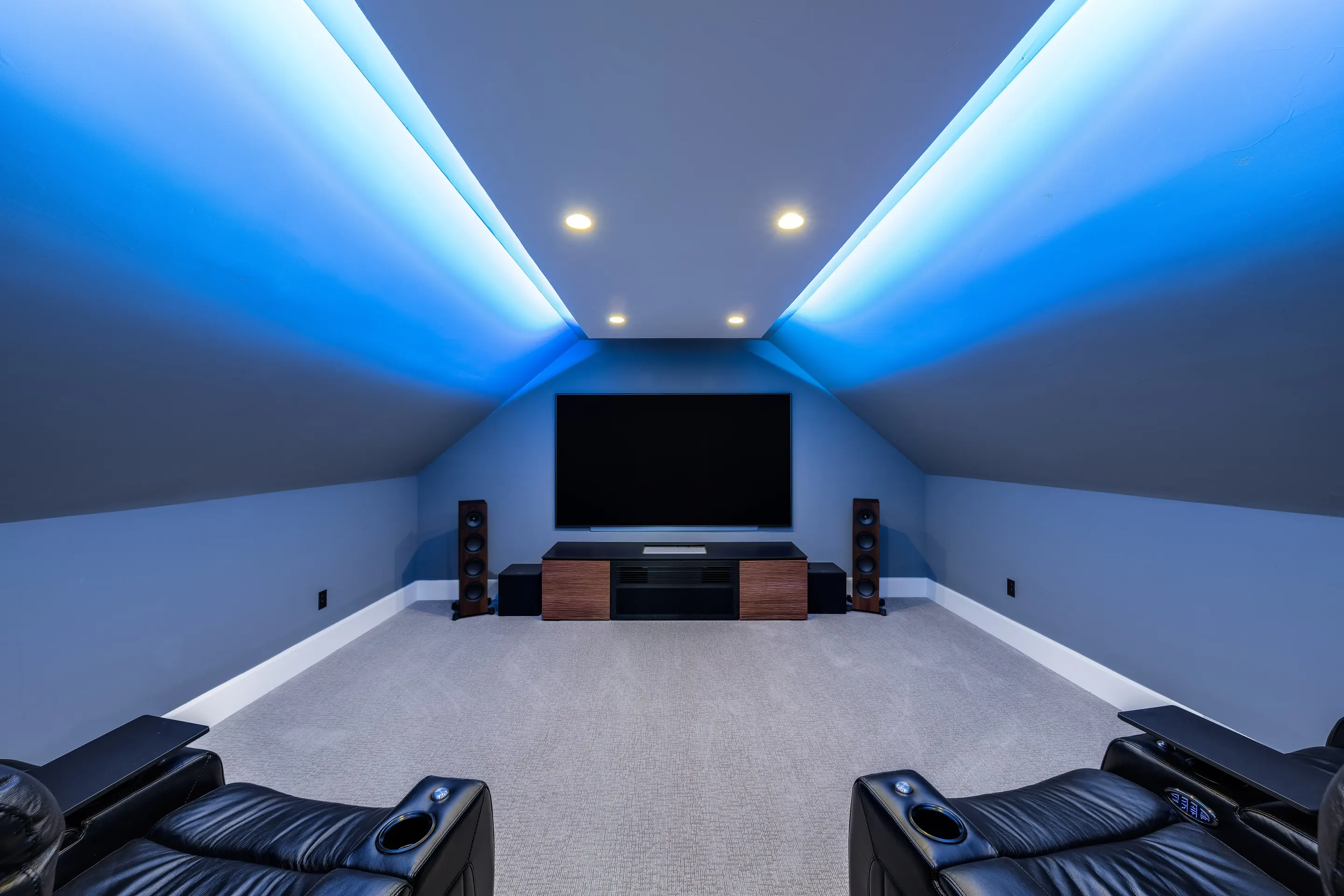 Media room with blue cove lighting, floorstanding speakers and reclining seating