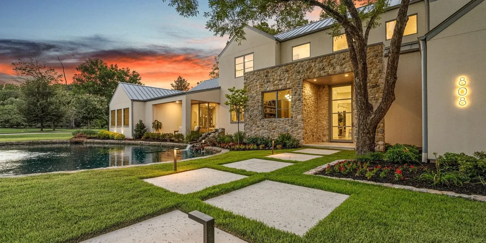 A custom residence at dusk with the facade, the path and the specimen tree separately lit, and the house number glowing beside the door
