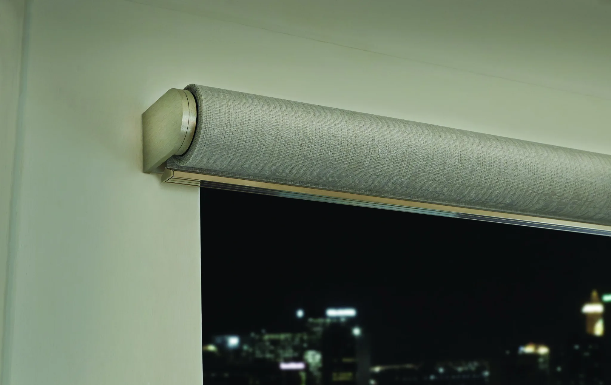 Palladiom — The exposed roller and end cap of a Palladiom shade, half lowered over a night city view