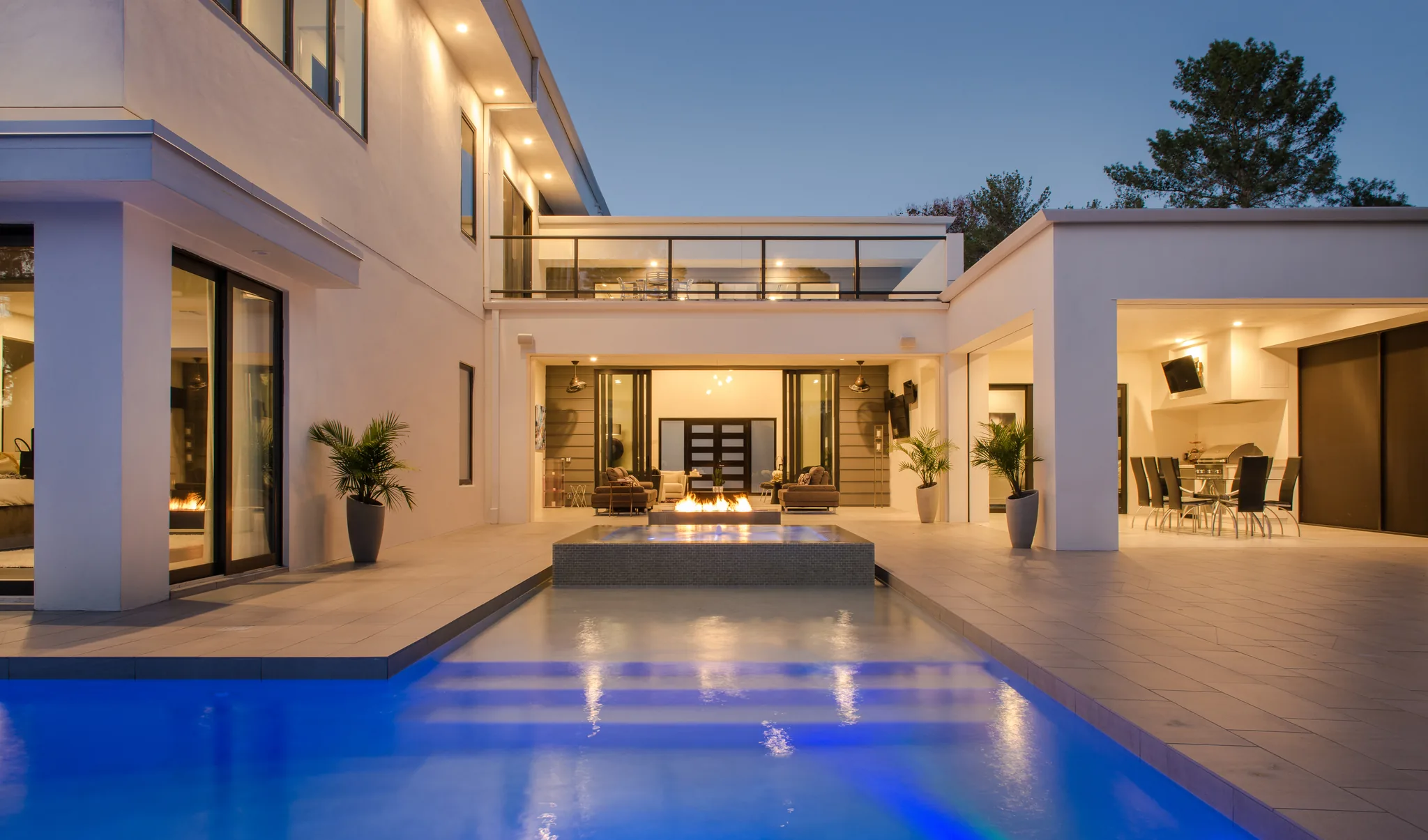 A lit courtyard and pool at dusk, the house glowing behind it
