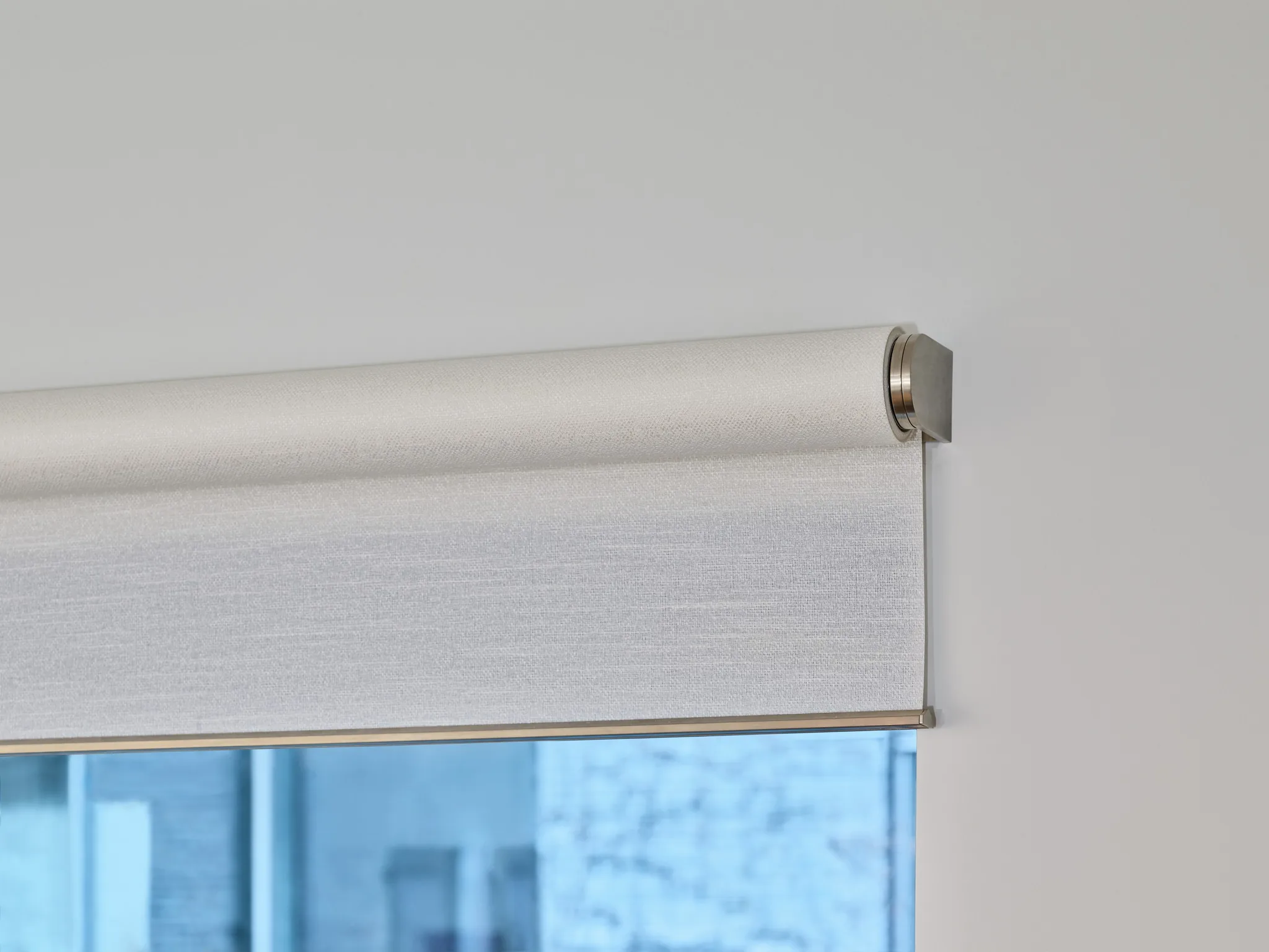 A roller shade and its bracket, seen close against a loft window