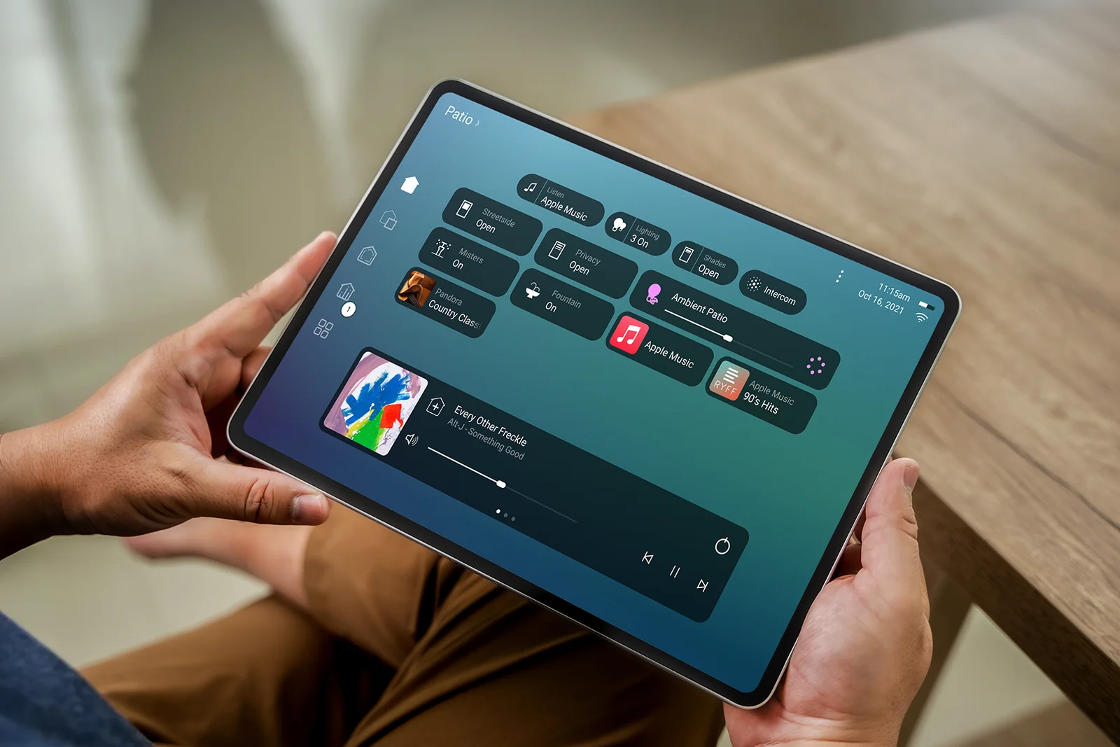 A tablet in hand showing a patio page with music, shades, lighting, misters and fountain controls